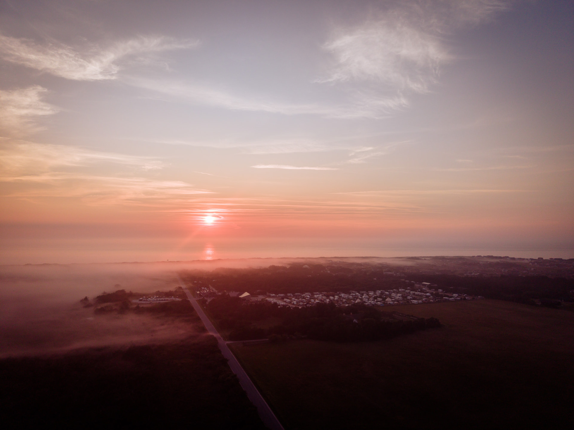 Dronefoto af solopgang over kystby i tåge